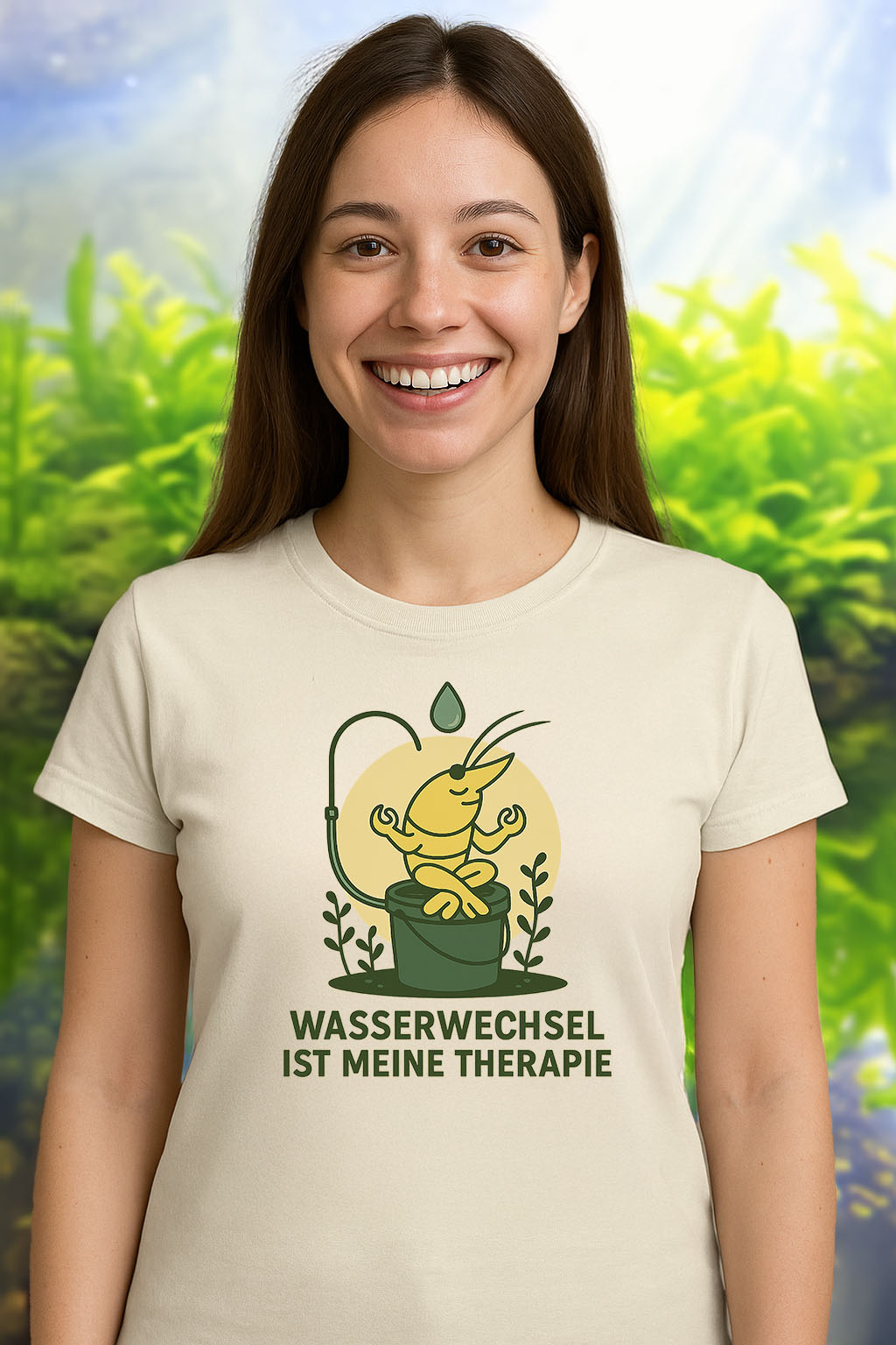 Eine junge Frau mit kastanienbraunen Haaren trägt ein naturweißes T-Shirt mit dem Aufdruck ‚Wasserwechsel Therapie‘. Das Motiv zeigt eine meditierende gelbe Garnele auf einem Eimer mit einem Wasserschlauch über dem Kopf. Die Frau lächelt freundlich in die Kamera, der Hintergrund ist neutral und weich.
